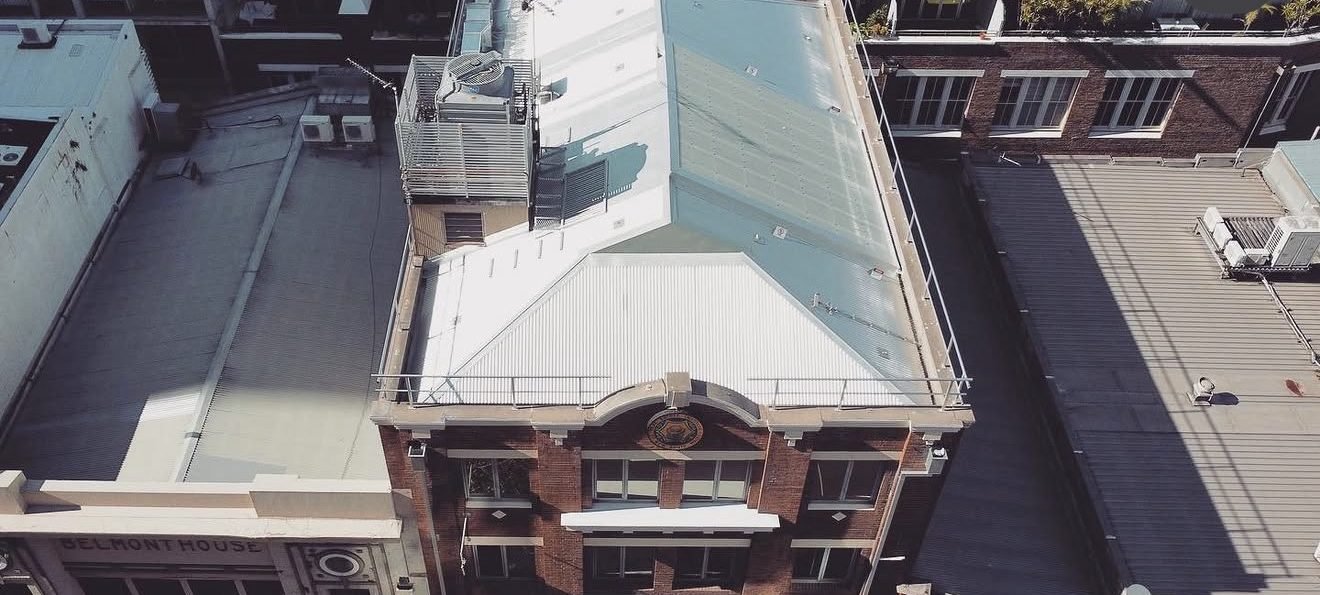 Aerial view of a red-brick heritage building with a newly reroofed metal hip roof